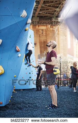 Stock Photo - Hispanic man looking up at outdoor climbing wall. Fotosearch