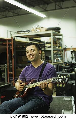 Stock Image - Hispanic man playing guitar in warehouse. Fotosearch