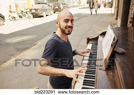 Stock Image - Hispanic man playing piano on city sidewalk. Fotosearch