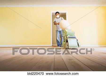 Stock Image - Hispanic man refinishing floors in new house. Fotosearch