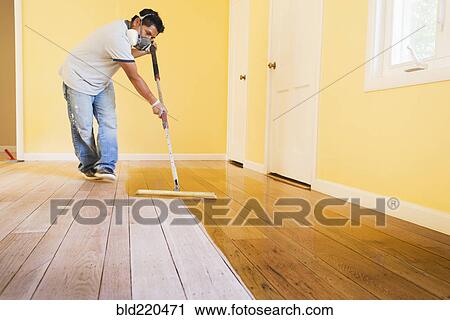 Stock Image - Hispanic man refinishing floors in new house. Fotosearch