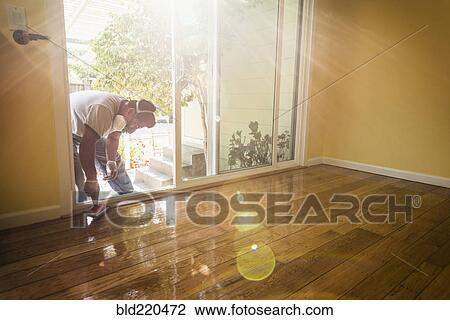 Stock Image - Hispanic man refinishing floors in new house. Fotosearch