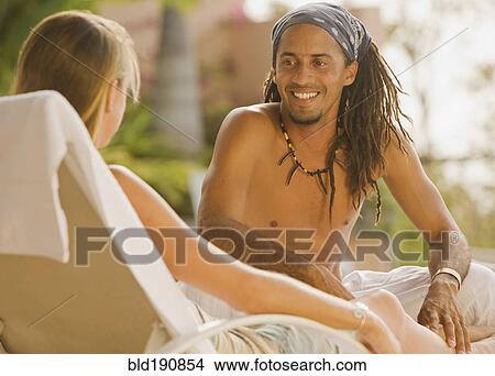 Picture - Hispanic man sitting on lounge chair talking to girlfriend. Fotosearch