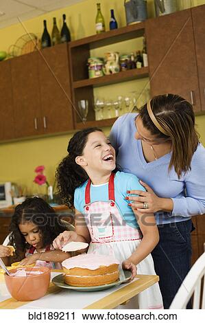 Stock Image - Hispanic mother and daughters baking cake. Fotosearch
