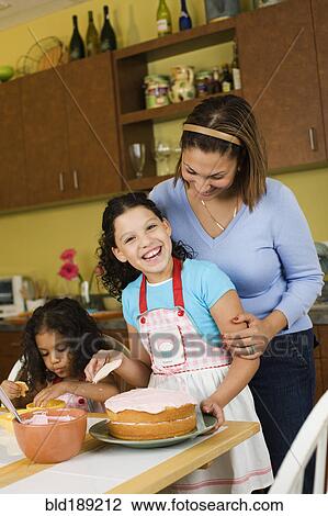 Stock Image - Hispanic mother and daughters baking cake. Fotosearch