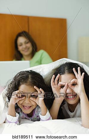 Stock Image - Hispanic sisters playing underneath blanket. Fotosearch