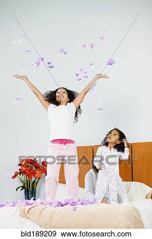 Stock Photo - Hispanic sisters throwing feathers in bedroom. Fotosearch