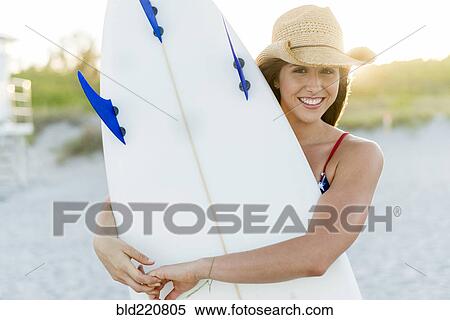 Stock Photography - Hispanic woman carrying surfboard on beach. Fotosearch