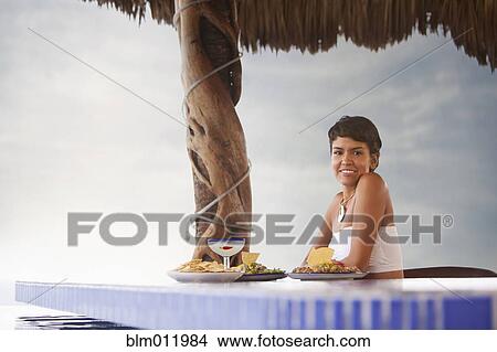 Picture - Hispanic woman having dinner at poolside. Fotosearch