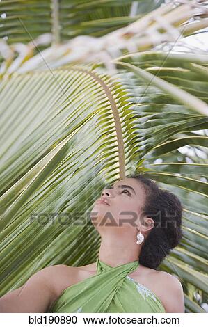 Stock Image - Hispanic woman in sarong near palm leaf. Fotosearch