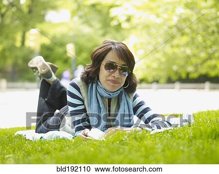Stock Image - Hispanic woman laying on blanket in grass. Fotosearch