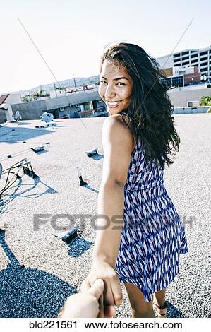 Stock Image - Hispanic woman pulling hand on urban rooftop. Fotosearch