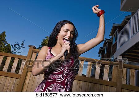 Stock Photo - Hispanic woman singing karaoke in backyard. Fotosearch