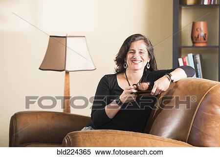 Stock Photography - Hispanic woman sitting in armchair drinking coffee. Fotosearch