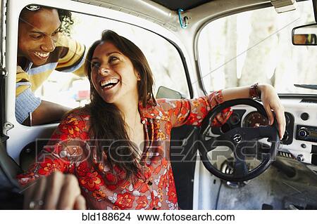 Picture - Hispanic woman sitting inside car laughing at friend. Fotosearch