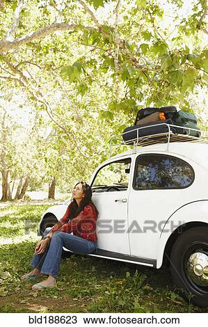 Stock Image - Hispanic woman sitting on side of car. Fotosearch
