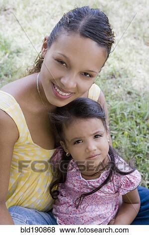Stock Photo - Hispanic woman sitting with daughter in lap. Fotosearch
