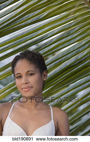 Stock Image - Hispanic woman standing near palm leaf. Fotosearch
