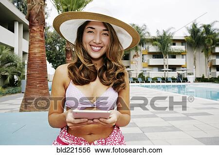 Stock Photograph - Hispanic woman using digital tablet at swimming pool. Fotosearch