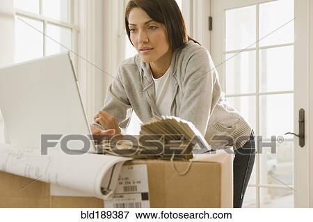 Stock Photo - Hispanic woman using laptop on boxes. Fotosearch