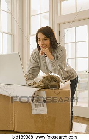 Stock Photo - Hispanic woman using laptop on boxes. Fotosearch