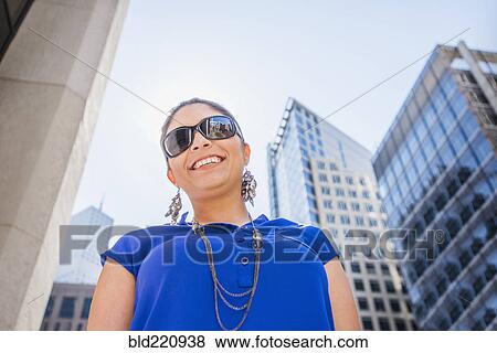Stock Photo - Hispanic woman walking under highrise buildings. Fotosearch
