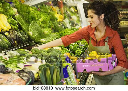 Stock Image - Hispanic woman working in produce section of grocery store. Fotosearch