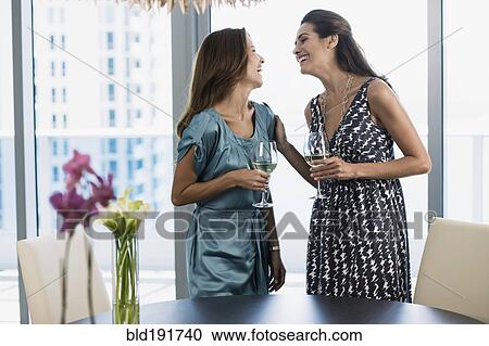 Stock Image - Hispanic women drinking white wine by window. Fotosearch