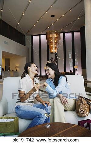 Stock Image - Hispanic women drinking white wine in hotel lobby. Fotosearch