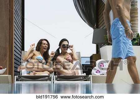 Stock Photograph - Hispanic women in bikinis eyeing passing man. Fotosearch
