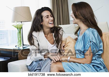 Stock Photo - Hispanic women laughing on sofa. Fotosearch