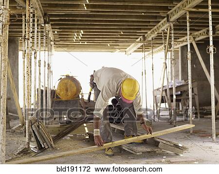 Stock Image - Hispanic worker measuring lumber at construction site. Fotosearch