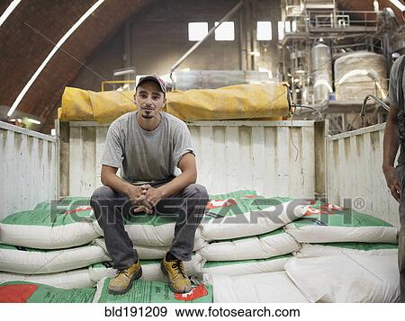 Stock Photo - Hispanic worker sitting on bag in factory. Fotosearch