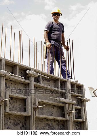 Stock Image - Hispanic worker standing on top of wall on construction site. Fotosearch