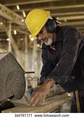 Stock Image - Hispanic worker using saw at construction site. Fotosearch