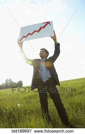 Stock Photo - Indian businessman holding up arrow graph in field. Fotosearch