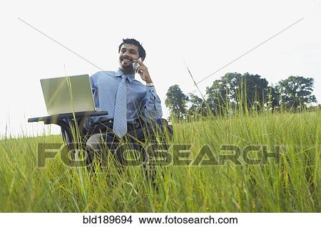 Indian businessman talking on cell phone in field View Large Photo Image Picture - Indian businessman talking on cell phone in field. Fotosearch