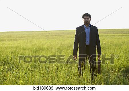 Stock Image - Indian businessman with briefcase in field. Fotosearch