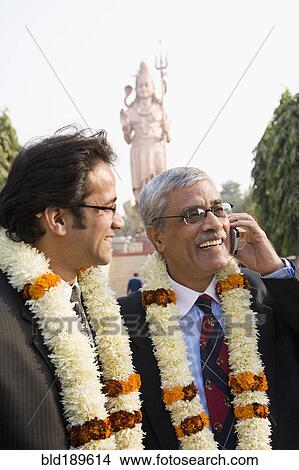 Picture - Indian businessmen wearing floral necklaces at tourist attraction. Fotosearch