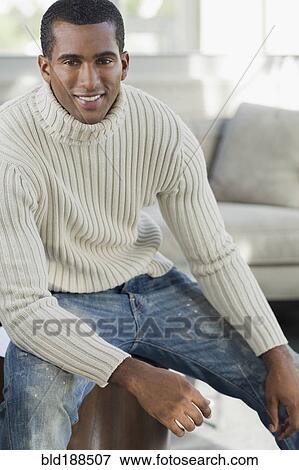 Stock Photo - Indian man sitting on edge of sofa. Fotosearch