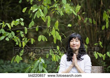 Stock Photo - Japanese woman meditating in garden. Fotosearch