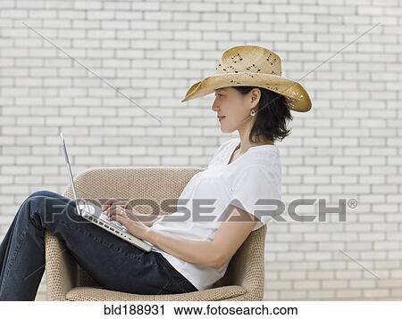 Stock Image - Japanese woman typing on laptop wearing cowboy hat. Fotosearch