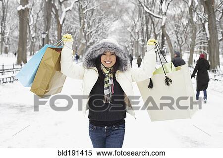 Stock Photography - Korean woman in snowy park carrying shopping bags. Fotosearch