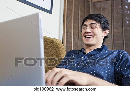 Stock Image - Laughing mixed race man typing on laptop. Fotosearch