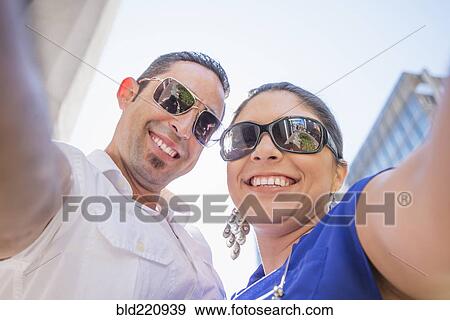 Stock Photo - Low angle view of Hispanic couple wearing sunglasses. Fotosearch