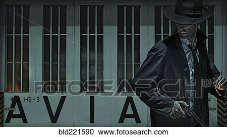 Stock Image - Man carrying gun near airport hangar. Fotosearch