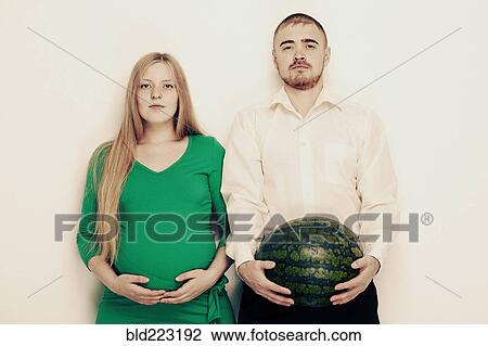 Stock Image - Man holding watermelon with pregnant girlfriend. Fotosearch