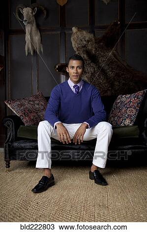 Stock Image - Man sitting on loveseat under trophy animals. Fotosearch