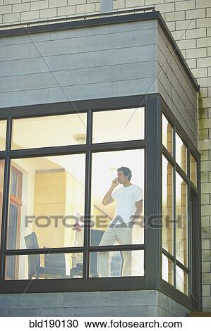 Stock Image - Man talking on cell phone next to window. Fotosearch