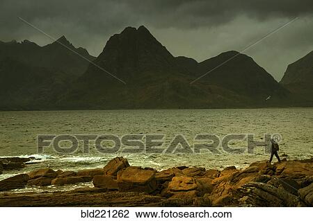Stock Image - Man walking on rocky beach. Fotosearch